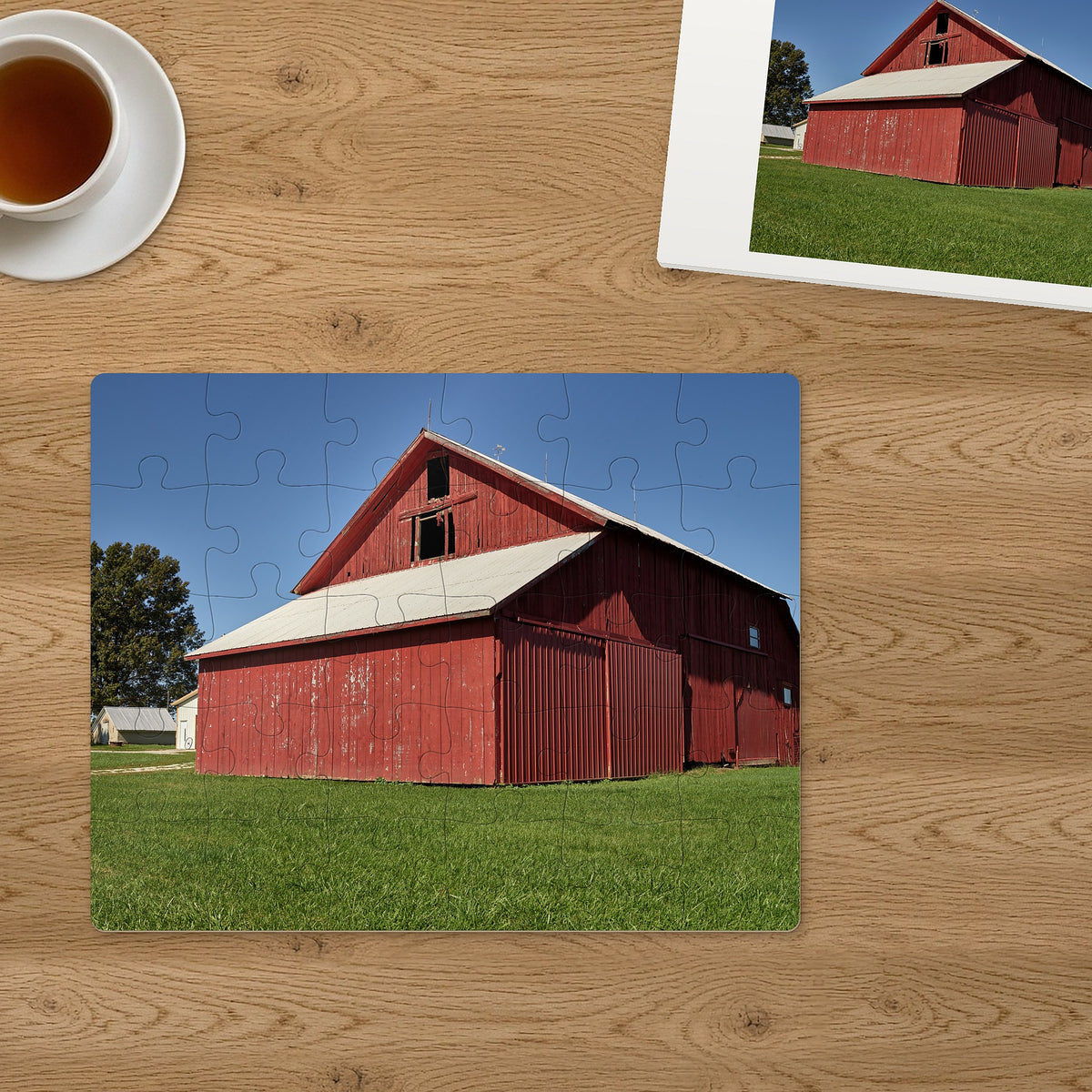 Memory Lane puzzle: Red Barn Morning. The finished 30-piece 14″ × 11″ puzzle on a table beside its white gift box (product illustration)